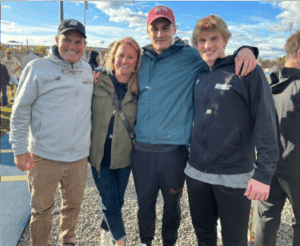Tyler stands next to his wife and two sons smiling in front of a blue sky.